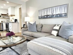 A modern living room with a grey sofa, a glass coffee table, and a painting of sailboats on the wall. - The Driftwood, Saint Andrews (St. Andrews)