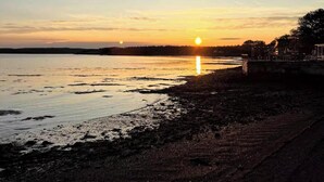 A sunset over a calm body of water with a shoreline and a distant tree line. - The Driftwood, Saint Andrews (St. Andrews)