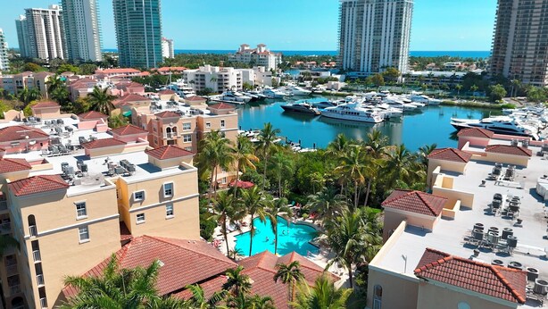 A marina with boats, a swimming pool surrounded by palm trees, and high-rise buildings in the background.