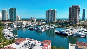 A marina with numerous yachts docked, surrounded by high-rise buildings and palm trees.