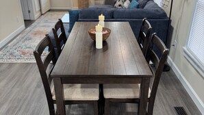 A dining area with a wooden table and chairs, a rug, and a bowl with candles. - Charming 2-bedroom house with AC, WiFi in the heart of Pembroke (Pembroke)