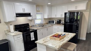 A modern kitchen with white cabinets, a black stove, a refrigerator, and a wooden island with a tray of snacks. - Charming 2-bedroom house with AC, WiFi in the heart of Pembroke (Pembroke)