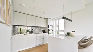 A modern kitchen with white cabinetry, a marble backsplash, and a central island. - Classy Modern Flat | Luxury & Comfy | Near Westfield & Tube (Greater London)