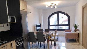 A modern kitchen with black cabinetry, a built-in microwave, and a stainless steel refrigerator. There is a dining area with a table and chairs, and a large arched window providing natural light. - PORTOCEL I (Marín)