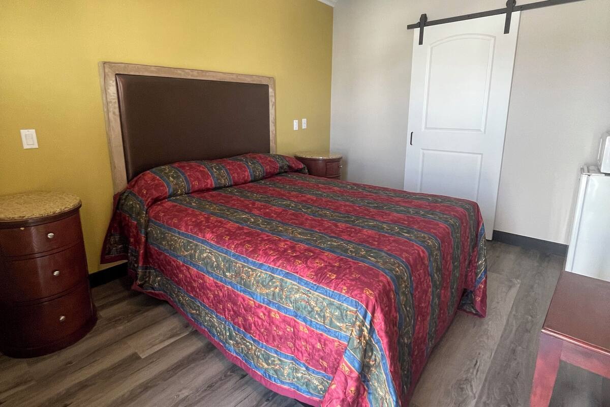 A bedroom with a bed, wooden nightstand, and a small table.