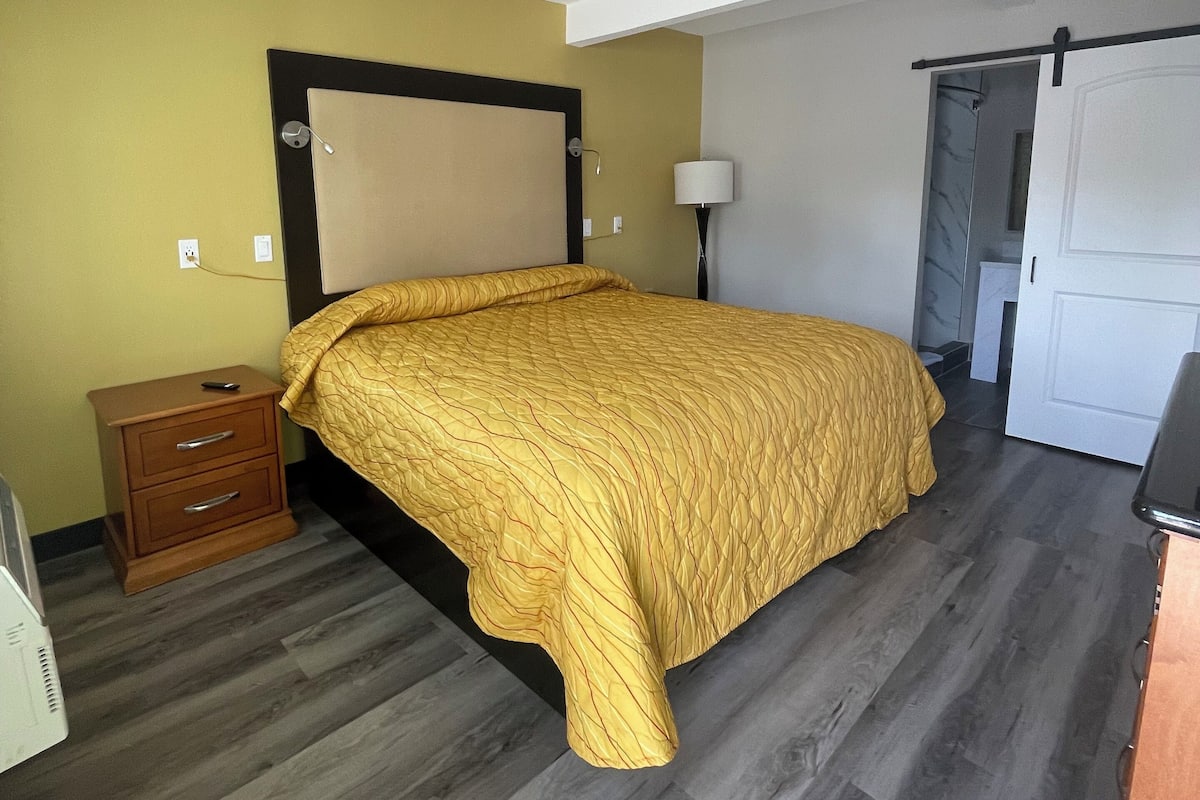 A bedroom with a bed, wooden nightstand, and a lamp.