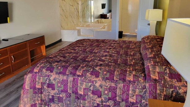 Une chambre à coucher avec un grand lit, une commode en bois, un miroir et une salle de bain visible à travers une porte ouverte.