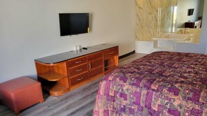 Une chambre à coucher avec un lit, une commode en bois, une télévision et un grand miroir.