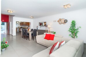 Een moderne woonkamer met een bank, eethoek en keuken op de achtergrond.