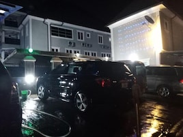 Uma área de estacionamento com veículos e um edifício com várias janelas e telhado plano.