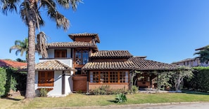 A two-story house with a tiled roof, a balcony, and a well-maintained lawn. - Bz46 Casa 150 metros da praia 5 suites (Buzios)