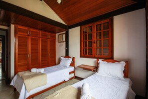 Une pièce avec deux lits en bois, une armoire en bois et une petite étagère en bois.