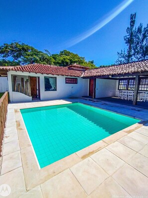 A swimming pool with tiled flooring, a building with a tiled roof, and a clear blue sky.