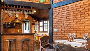 A restaurant interior with brick walls, wooden bar stools, and a dining table set with plates and glasses. - Bz46 Casa 150 metros da praia 5 suites (Buzios)