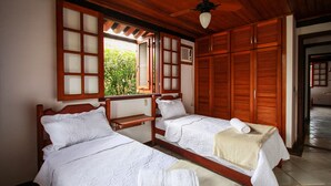 Una habitación con dos camas de madera, un ventilador de techo y una ventana que da a zonas verdes.