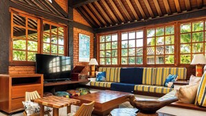 A cozy living room with a television, wooden furniture, and large windows. - Bz46 Casa 150 metros da praia 5 suites (Buzios)