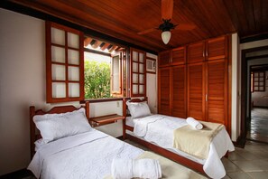 A room with two wooden beds, a ceiling fan, and a window with a view of greenery.