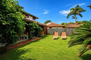 Un jardin avec une terrasse, deux chaises longues, une clôture en bois et un palmier.