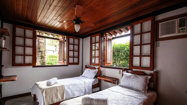 A room with two beds, wooden ceiling, and large windows with wooden frames. - Bz46 Casa 150 metros da praia 5 suites (Buzios)
