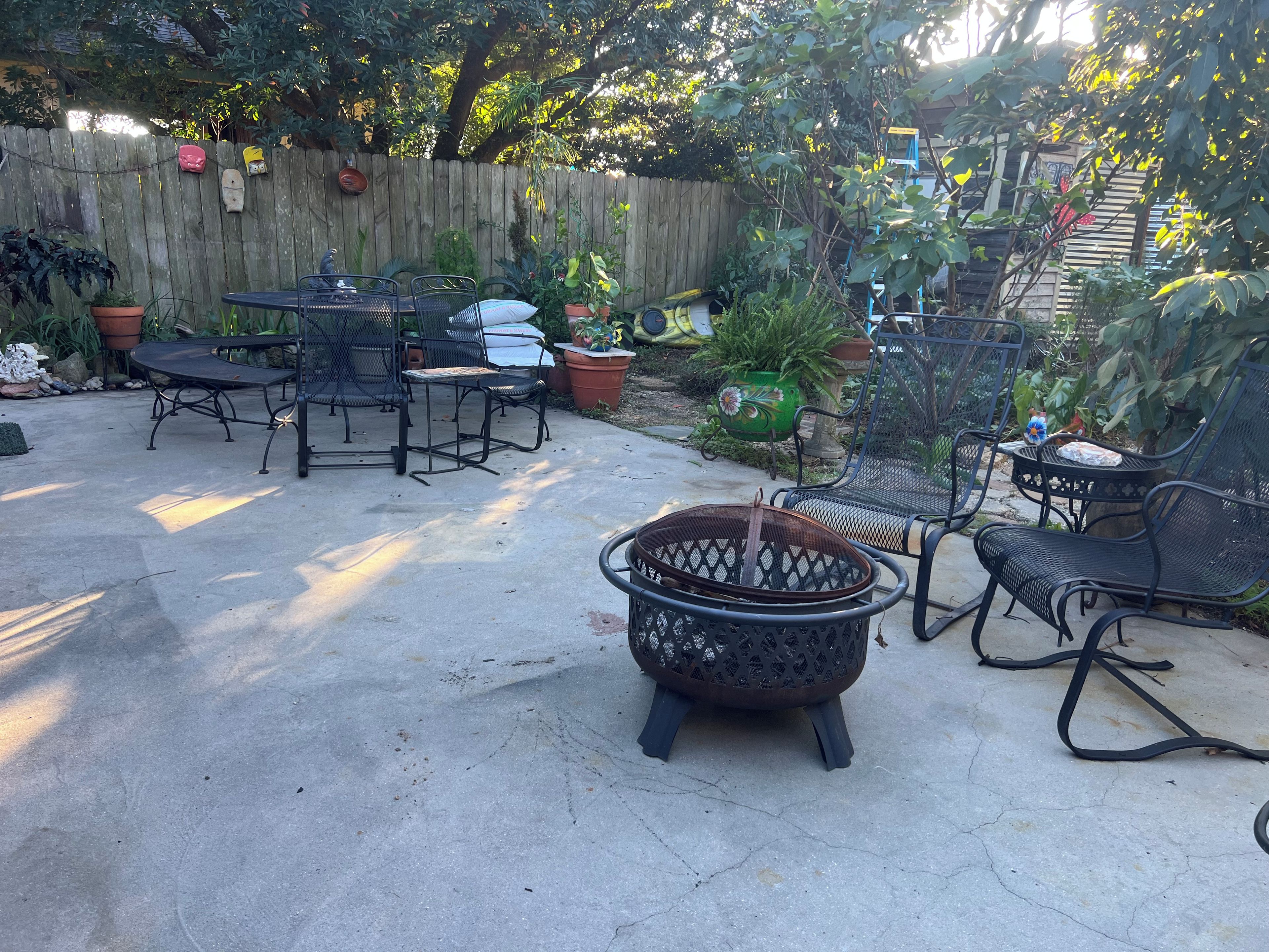 Un patio al aire libre con una mesa redonda y sillas, rodeado de plantas en macetas y una valla de madera.