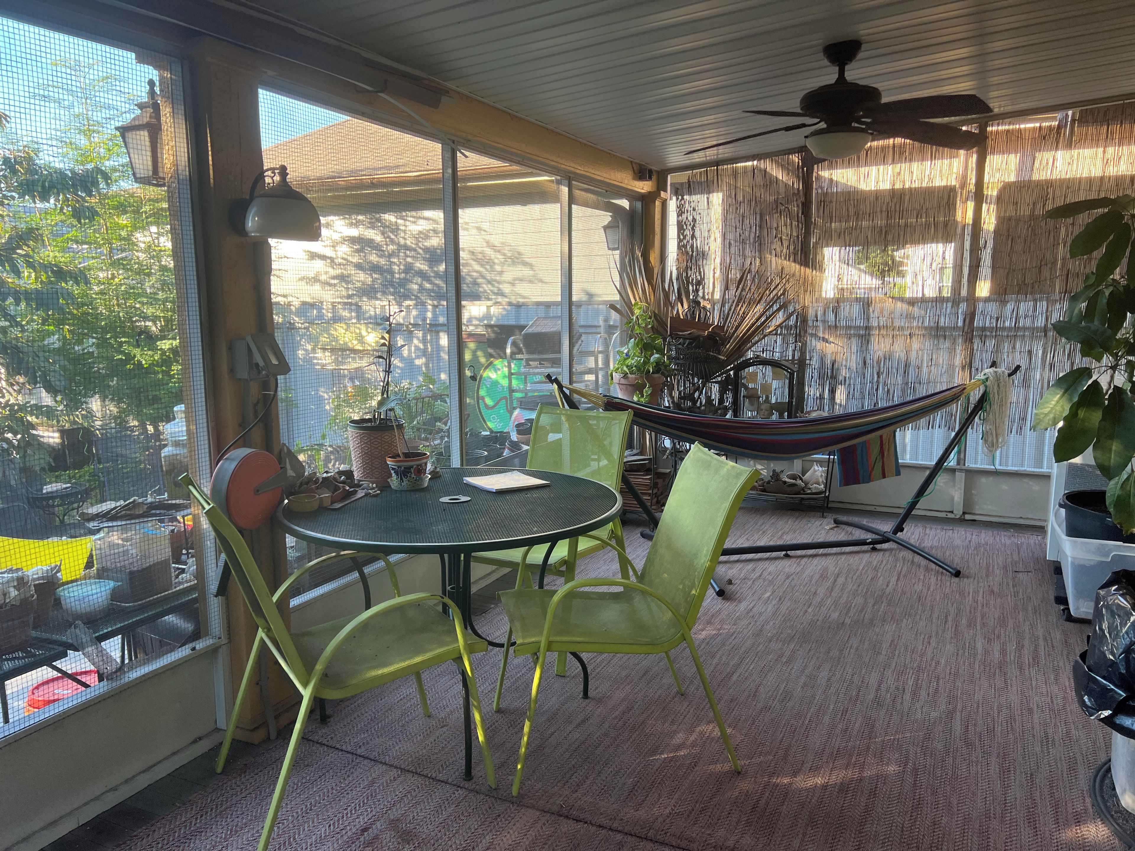 A sunlit patio with a table, chairs, a hammock, and potted plants.