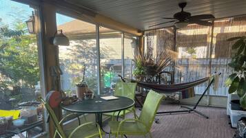 A sunlit patio with a table, chairs, a hammock, and potted plants.