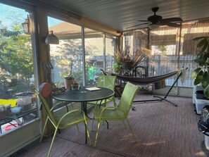 A sunlit patio with a table, chairs, a hammock, and potted plants. - Charming bungalow in Arabi (Arabi)