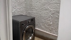 A compact laundry room with a front-loading washing machine, a textured wall, and a tiled floor. - Stylish apartment in laurels, premium location! (Medellín)