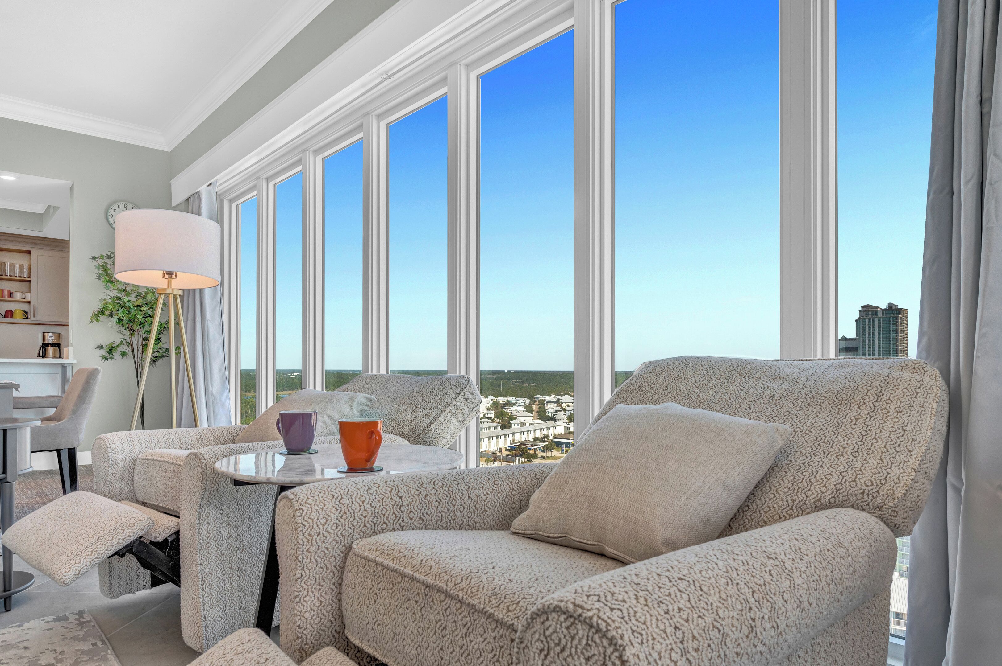 Ein modernes Wohnzimmer mit Sofa, Couchtisch und Lampe. Große Fenster bieten Blick auf die Stadtlandschaft.