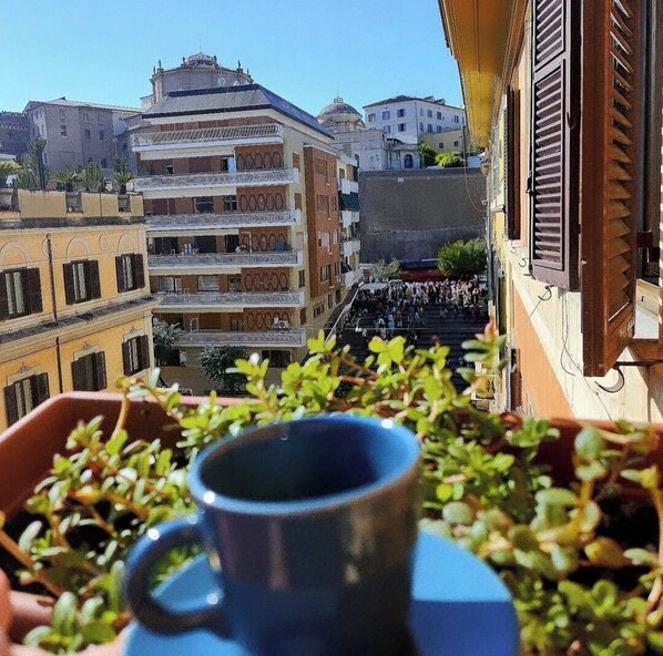 Un balcón con vistas a un paisaje urbano, que incluye un edificio con varios balcones y una multitud en la calle de abajo.