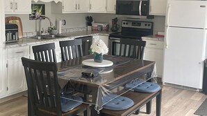 A modern kitchen with white cabinets, a black microwave, a white refrigerator, and a dining table with chairs. - Beautiful, cozy, spacious suite located central PEI. 3 bedrooms 4 beds.  (Lot 67)