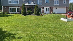 A two-story house with a large front lawn, a garage, and a balcony. - Beautiful, cozy, spacious suite located central PEI. 3 bedrooms 4 beds.  (Lot 67)