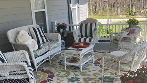 A covered porch with wicker furniture, a floral rug, and a view of a yard with trees and a bicycle. - Family-friendly close to SDC, Branson, Eureka Springs, Table Rock, Roaring River (Cassville)