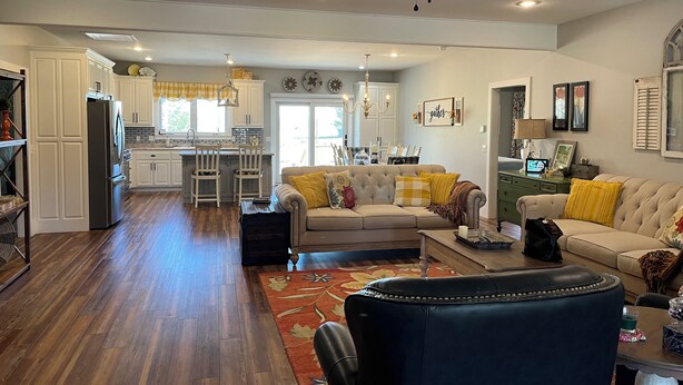 A spacious living room with a sofa, a coffee table, and a dark leather chair. There is a kitchen area with white cabinets and a refrigerator. - Family-friendly close to SDC, Branson, Eureka Springs, Table Rock, Roaring River (Cassville)