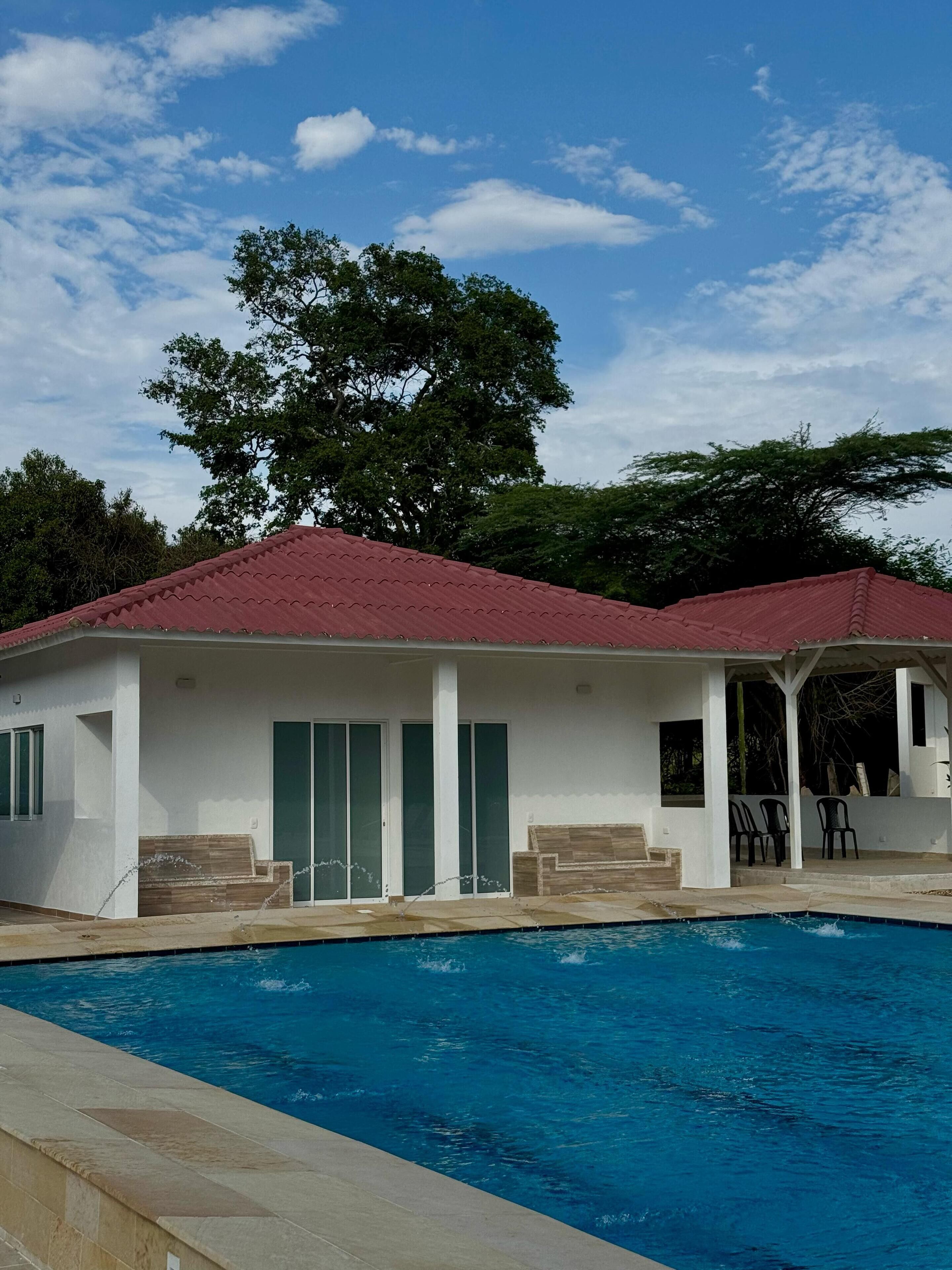 A modern building with a swimming pool, featuring a red roof, large windows, and a covered patio area.