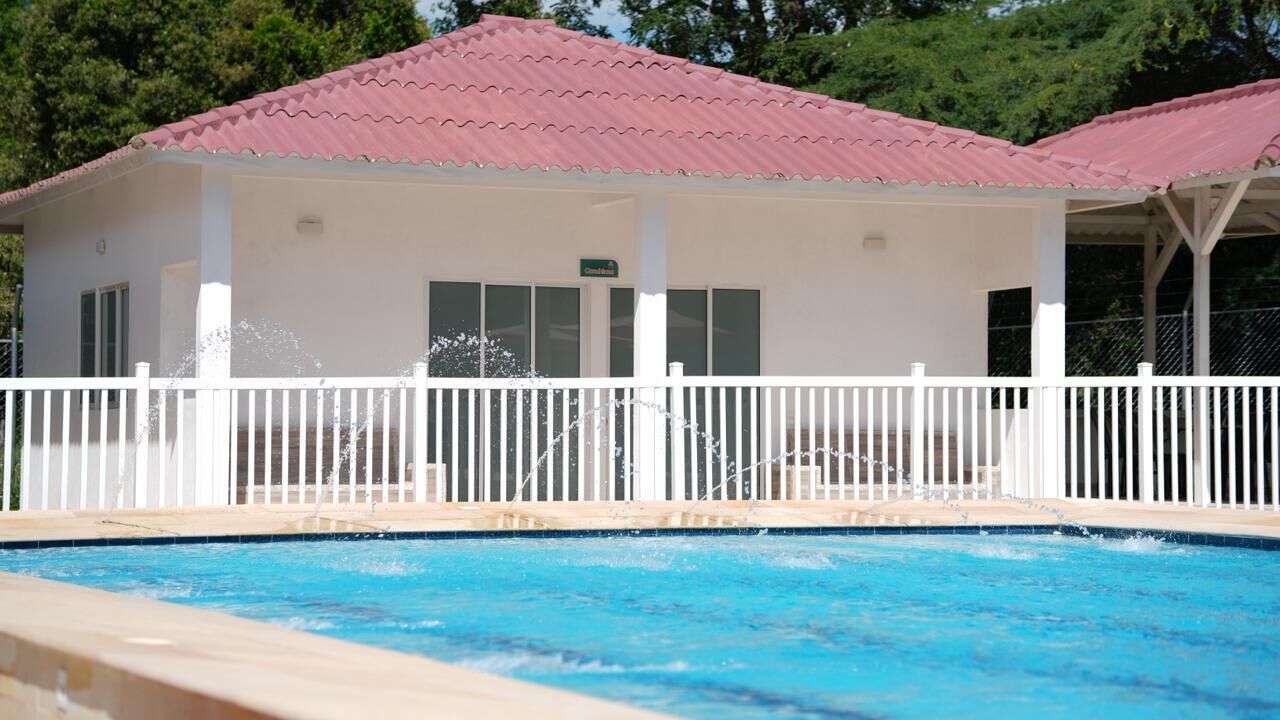 A poolside building with a red roof, white exterior walls, and a white fence.