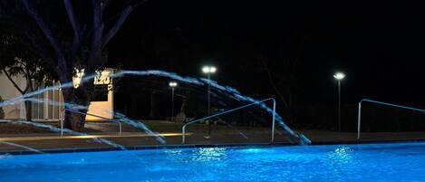 A nighttime swimming pool with water features and lighting.