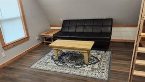 A loft-style room with a black leather sofa, a wooden coffee table, and a patterned rug on a wooden floor. - Cedar Grove Rental A-frame (Clarksville)