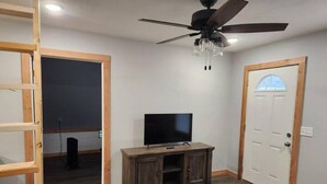 A room with a ceiling fan, a TV on a wooden cabinet, and a door with a window. - Cedar Grove Rental A-frame (Clarksville)