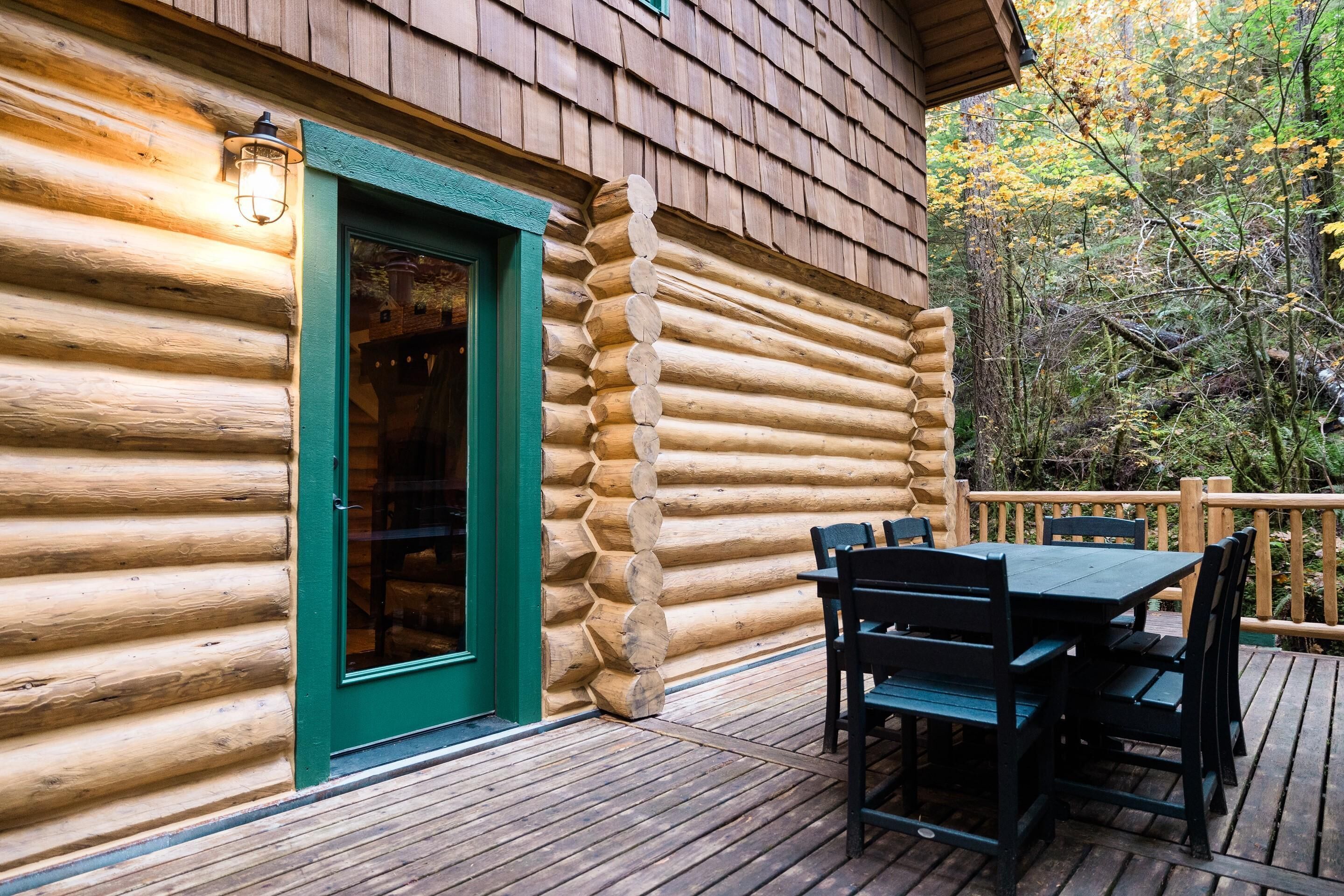 Uma cabana de tronco com porta verde e um deck com mobiliário de exterior.