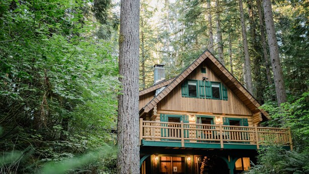 Une cabane en bois dotée d’un balcon, entourée d’une forêt dense.