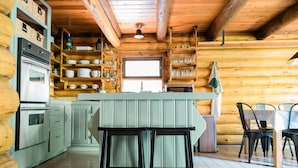 Une cuisine rustique aux murs en bois, dotée d’un four encastré et d’un îlot central avec des tabourets.