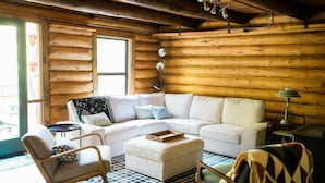 L’intérieur d’un chalet confortable, avec des murs en bois, un canapé d’angle, un fauteuil à bascule et un tapis à motifs.