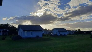 A row of single-story houses with a grassy field in the foreground and a cloudy sky in the background. - Cabañas Eden Soñado (Tandil)