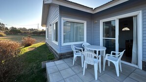 A modern house with a patio featuring a table and chairs, large windows, and a view of a grassy field. - Cabañas Eden Soñado (Tandil)