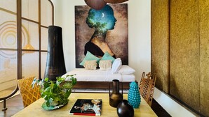 Una habitación con cama, ventilador de techo, televisor montado en la pared, estantería y un cuadro decorativo.