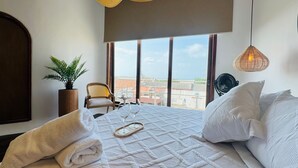 Habitación de hotel con una cama grande, una planta en maceta, una silla y vistas a la ciudad.