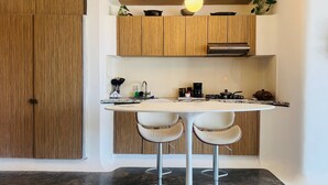 Una cocina moderna con armarios de madera, una mesa de comedor redonda, dos taburetes de bar y una cafetera.