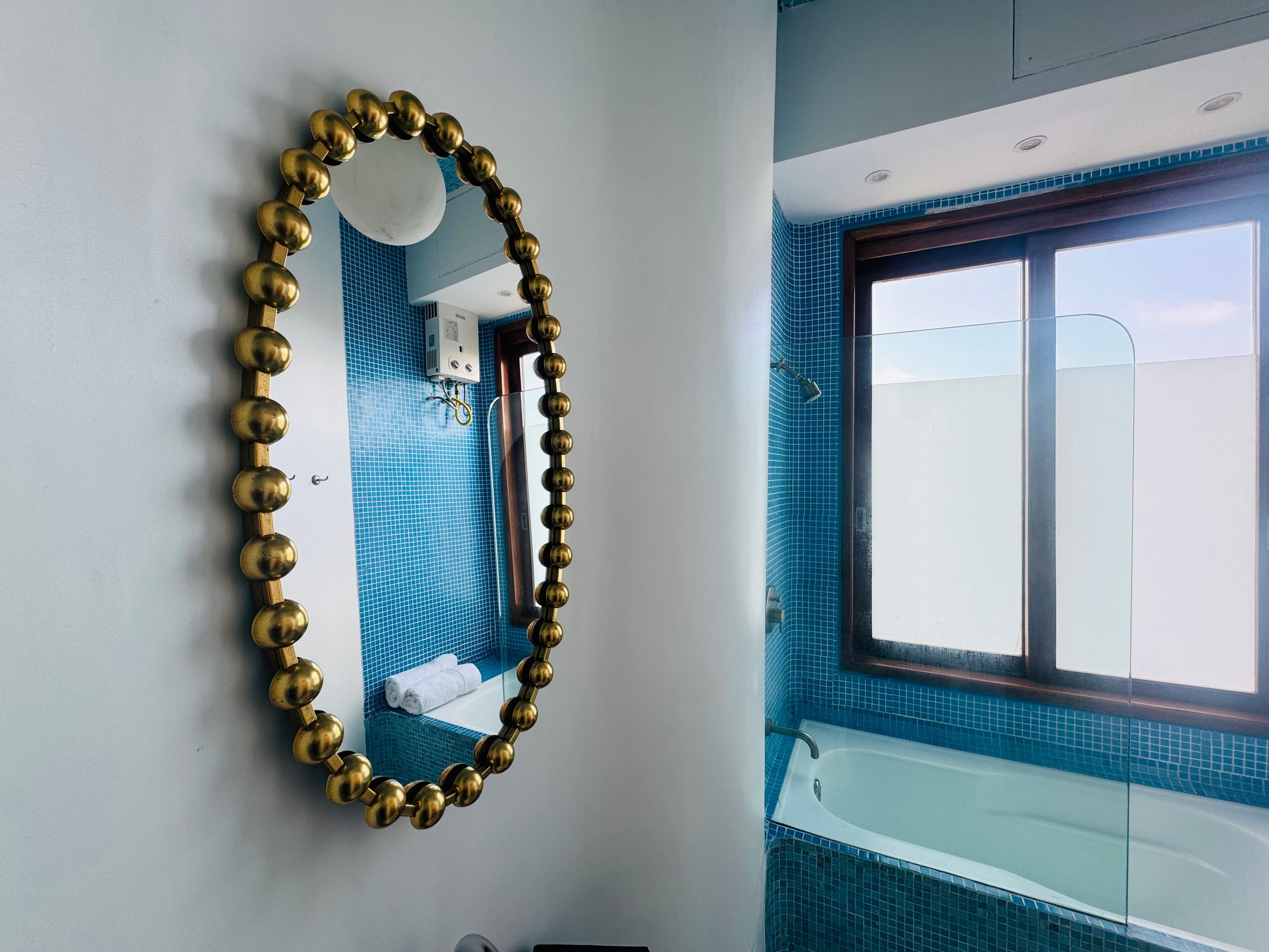 Een badkamer met een bad, een blauwe betegelde muur en een spiegel met gouden lijst.