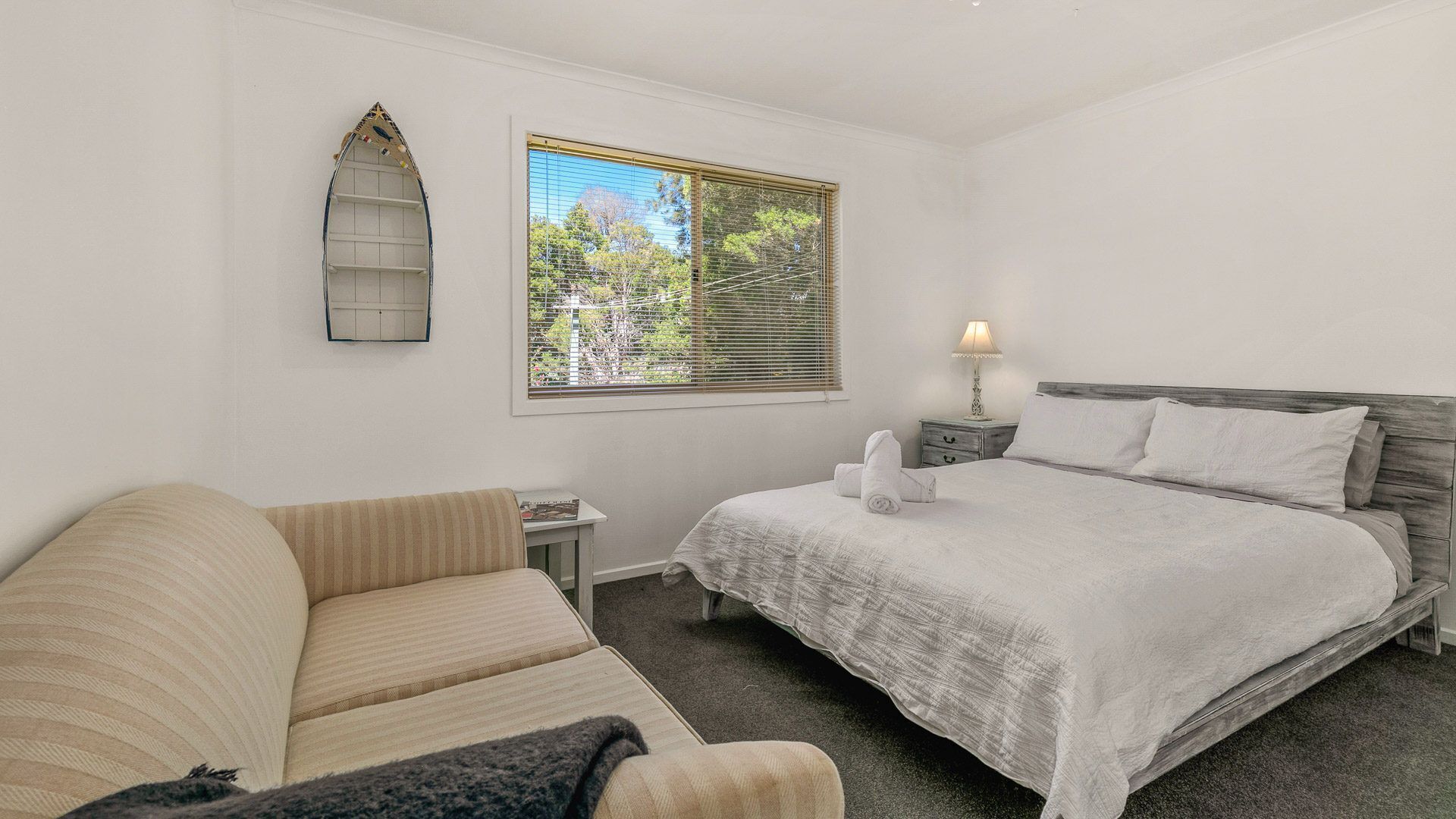 A bedroom with a bed, a sofa, a nightstand, a lamp, and a window with blinds.